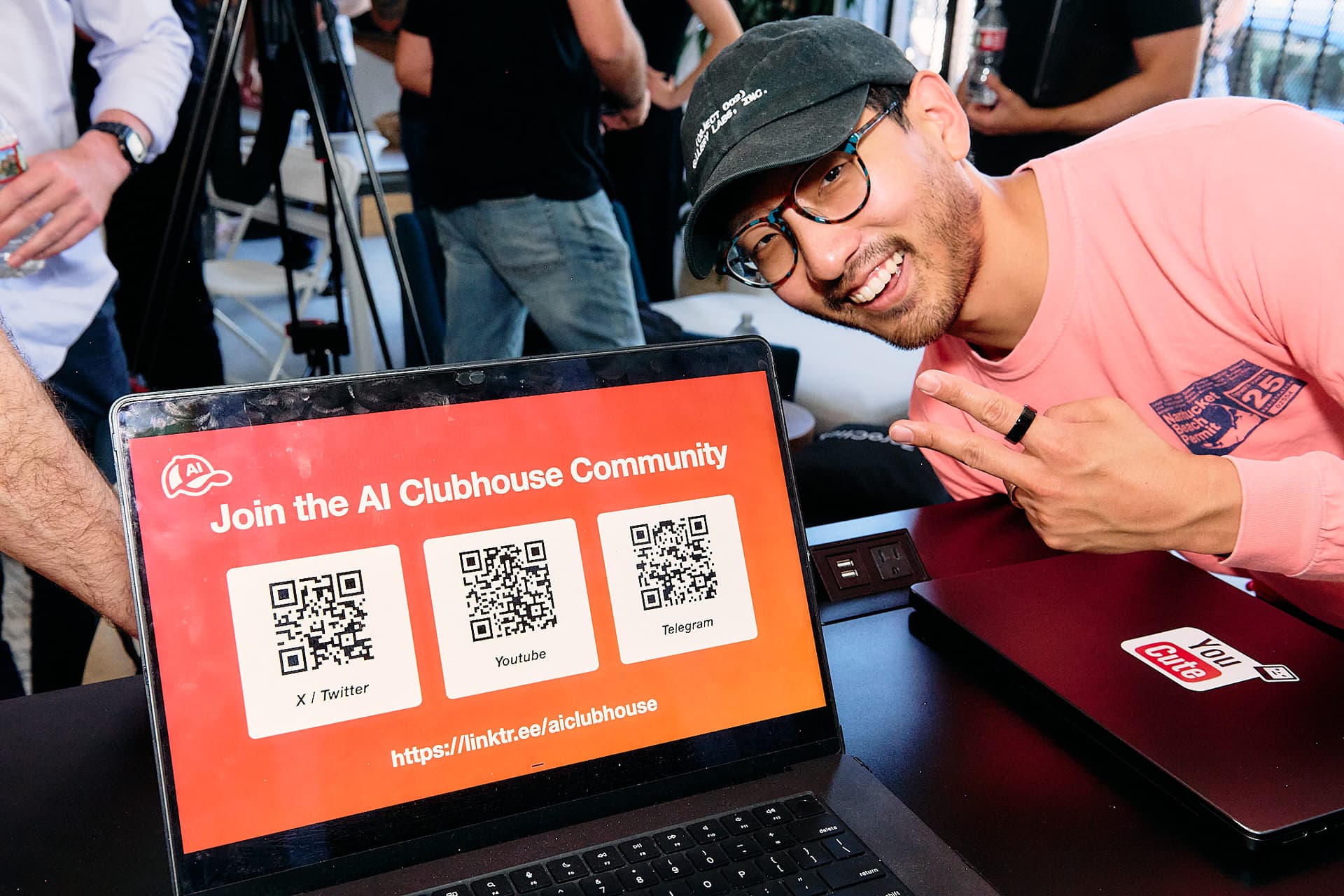 An attendee posing next to a laptop showing the AI Clubhouse community QR codes
